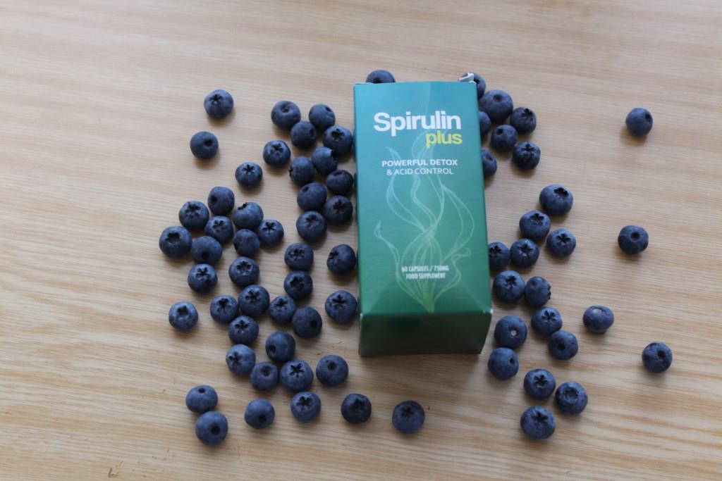 Spirulin Plus 10 medicine bottle packaging on a table surrounded by blueberries