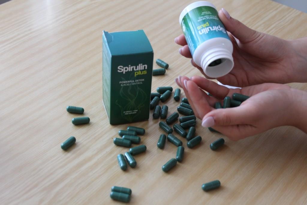 Spirulin Plus 11 medicine bottle packaging on a table surrounded by pills